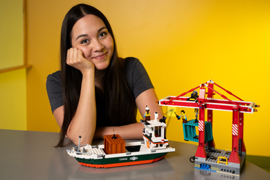 Chelsea Mitchell smiles next to Lego set showing a shipping port with a crane putting containers on a ship.