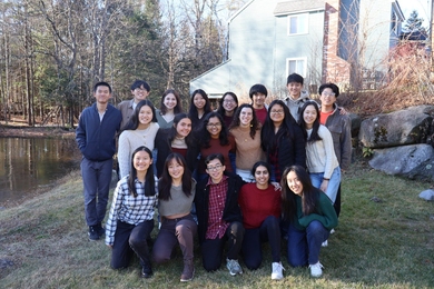 19 people pose outdoors in three rows on a spring day
