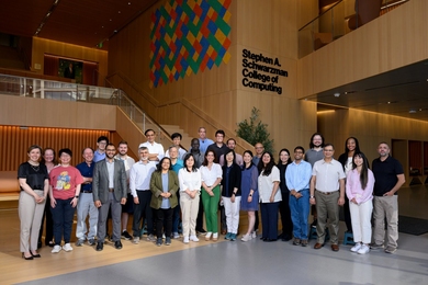 29 people pose for a group photo in the MIT Schwarzman College of Computing lobby.