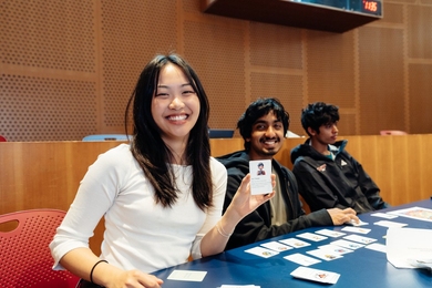 A student holds up a printed card containing a reminder of a skill learned in class. Two other students sit next to her.