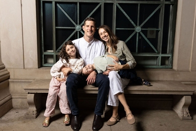 Portrait of a smiling couple on a stone bench, with their daughter leaning against her dad, and their young son sprawled across the laps of both parents.
