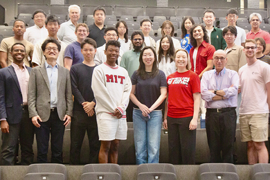27 people stand together in rows of an auditorium and pose for a picture