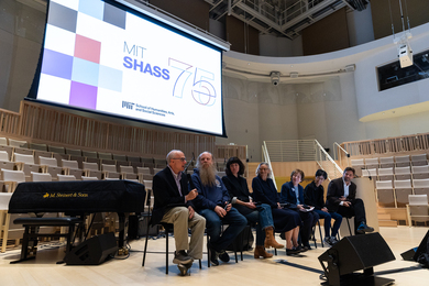 In an auditorium, 7 professors sit in a line beneath a large screen that says SHASS 75 