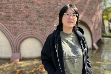 Angeline Peng, poses, standing in front of the circular brick MIT Chapel on a sunny day