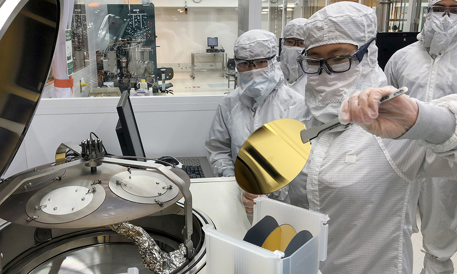 Photo of four people in clean suits preparing to load a golden disk into a large piece of lab equipment