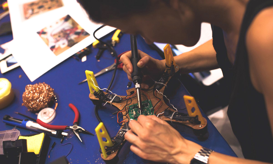 A person solders a circuit board on the underside of a drone-type device.