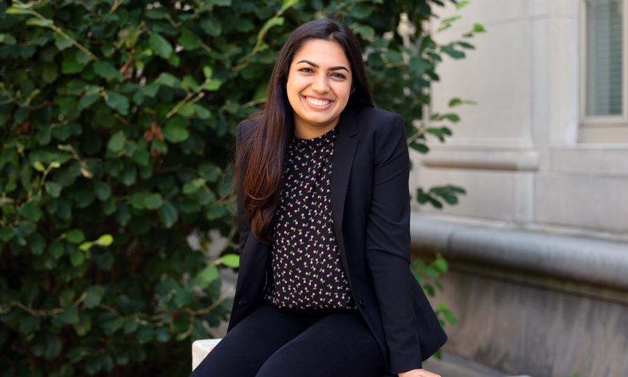 Avni Singhal sits outside on MIT campus and smiles. A peek of an MIT building is in the background.