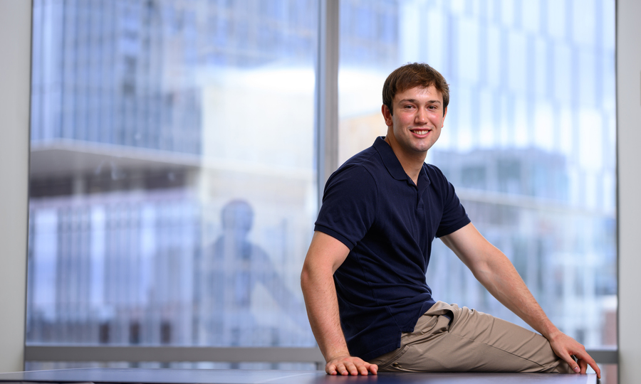 James Simon smiles while sitting on a ping pong table, with windows in background.