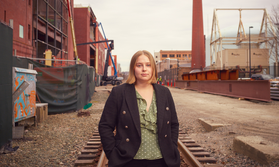 Mikayla Britsch stands on railway tracks near MIT campus, with buildings in background.