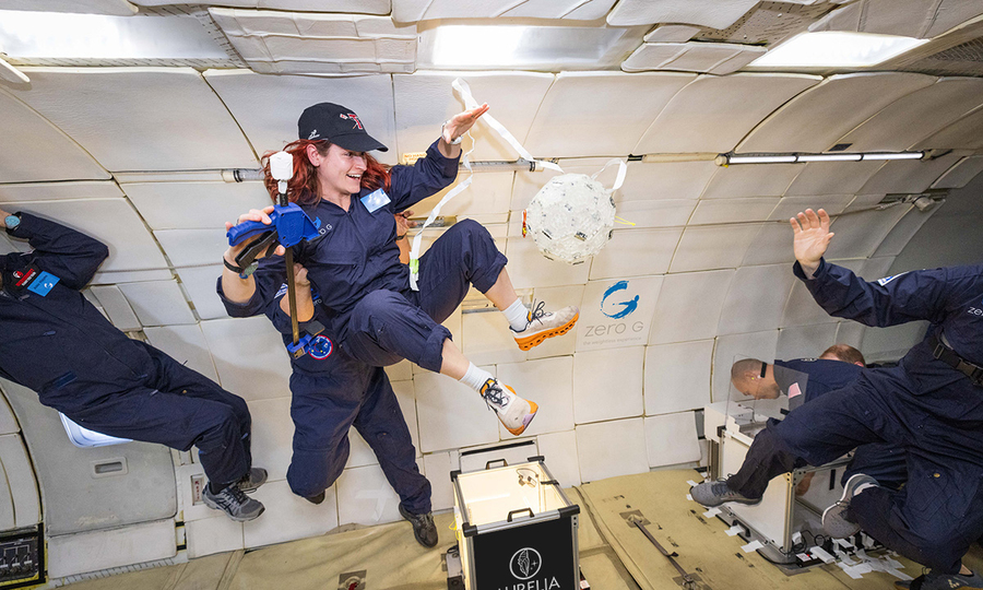 Five people in blue suits float in zero-gravity.