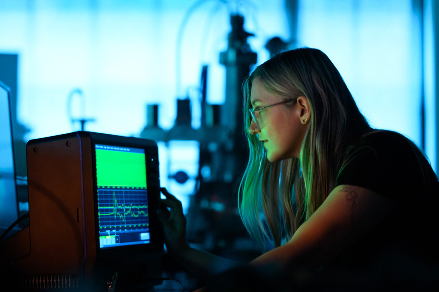 Lanie McKinney looks at glowing green waveforms on an oscilloscope in the lab.