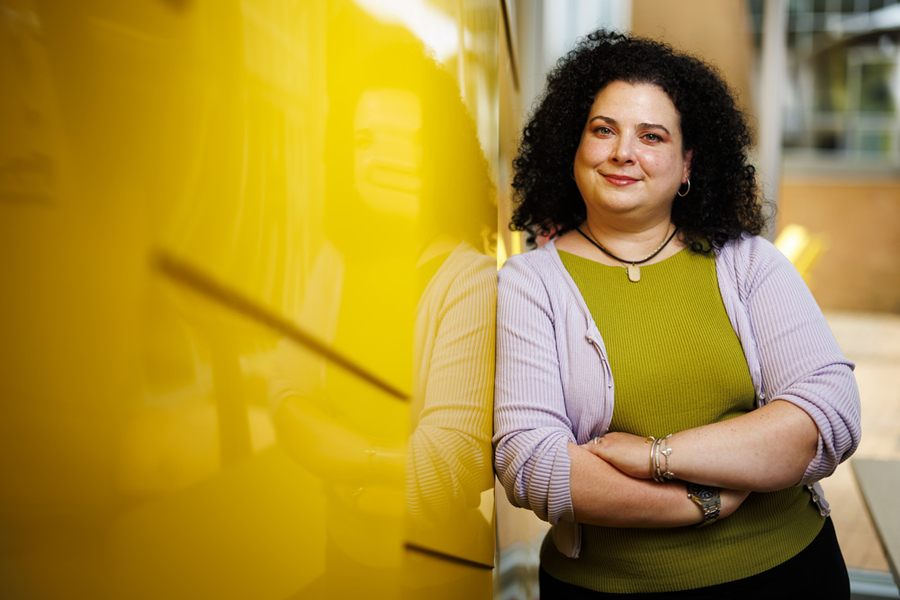 Christina Delimitrou leans against a yellow wall outside of Stata Center.