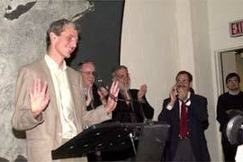 Professor Wolfgang Ketterle unsuccessfully tries to still the applause that greeted him at the MIT news conference about his Nobel Prize. Behind him are (left to right) President Charles M. Vest, Dean of Science Robert Silbey and Professor Marc Kastner, head of the physics department.