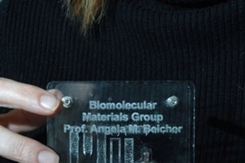 Angela Belcher holds a display of the virus-built battery she helped engineer. The battery -- the silver-colored disc -- is being used to power an LED.