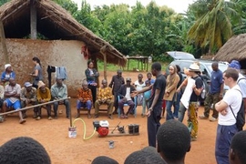 Members of a team that developed a system for generating gas from agricultural waste, which is attached to a small engine to generate power for charging cellphones, demonstrate their prototype at a village in Ghana.