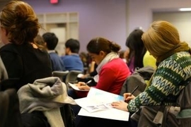 Half a dozen people sit in small desks during a workshop