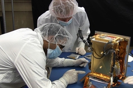 MIT graduate students Pronoy Biswas (left) and Mark Chodas prepare the REgolith X-Ray Imaging Spectrometer (REXIS) instrument for flight.