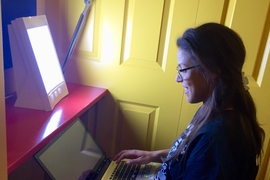 A fourth-year PhD student in electrical engineering and computer science, Ariel Anders works beside a light-therapy box recently installed at MIT.