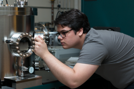 Summer Scholar Grant Smith looks into a sputter deposition chamber, where he makes ultrathin films — from 2 to 10 nanometers thick — of magnetic materials suitable for spin-based electronics such as those used in computer memory systems.