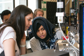 Summer Scholar Abigail Nason (left) and graduate student Takian Fakhrul peer into a pulsed laser deposition chamber for creating thin films that combine magnetic properties and infrared light transparency to serve in waveguides and isolators for integrated photonic chips.