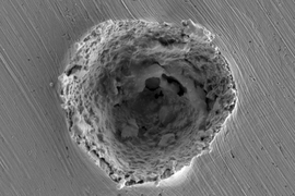 This scanning electron micrograph shows the crater left by the impact of a 10-micrometer particle traveling at more than 1 kilometer per second. Impacts at that speed produce some melting and erosion of the surface, as revealed by this research.