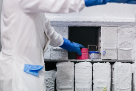 Photo of a gowned lab worker putting samples in the freezer