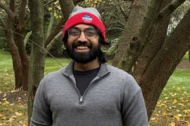 Photo of Ashwin Narayan standing near some trees wearing an "I voted" knit hat