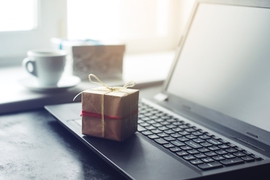 Photo of a small box, gift-wrapped in paper and twine, sitting on a laptop