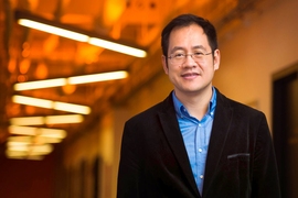 Photo of Ju Li standing in a hallway with linear ceiling lights, hung in "v" shapes
