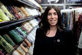 Photo of Stephanie Benedetto surrounded by rows and racks of textiles