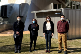 A photo of four people standing outside the Stata Center, wearing facemasks