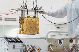 MOXIE hangs over the Perseverance rover in a NASA cleanroom, as a person in a cleansuit guides it