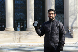 Meshkat Botshekan standing in front of MIT, holding up a smartphone