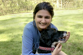 photo portrait of Natasha Joglekar, kneeling on a lawn and holding a dog