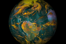 An image of Earth in false color, with the oceans bluish green, lands green and yellow and purple, and clouds yellowy orange