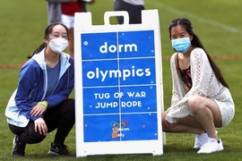 Photo of Ellie Feng and Ashley Ke crouching on either side of a sign that reads "Dorm Olympics: tug of war and jump rope"
