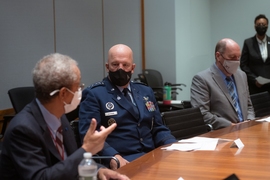 Photo of three men wearing facemasks and sitting at a table, with another indivdiual standing in the background