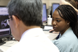 Photo of Demilade Adedinsewo looking at a computer monitor with an unidentified man sitting to her left