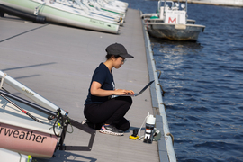 Charlene Xia kneeling on a dock, facing the water and typing on a laptop.