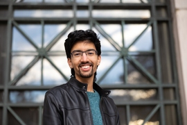 Photo of a student standing with an MIT wall of windows behind him.