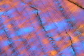 Electron microscope image of granitic nanocrystals, which looks like black fault lines in an orange material that's covered with wispy areas of blue