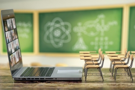 Photo of two rows of miniature desks in front of an open laptop, with blurred chalkboards in the background