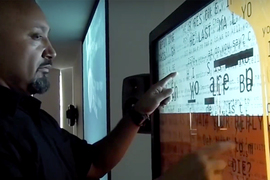 Video-captured image of a man studying data on a wall-mounted screen
