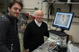 Photo of two smiling men standing at a lab bench covered with electronic equipment