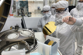 Photo of four people in clean suits preparing to load a golden disk into a large piece of lab equipment