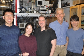 Photo of five people standing before racks of electronic equipment and smiling
