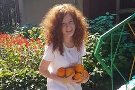 Photo of Yulia Zdanovska standing in front of a garden, holding oranges.