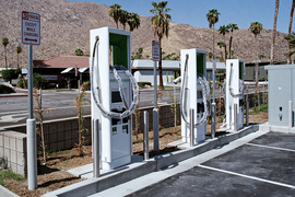 Photo of an electric vehicle charging station in the desert with dry rolling hills and a few palm trees in the background
