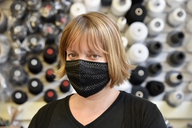 Photo of Lavender Tessmer wearing a black face mask in front of a wall full of spools of black and white thread