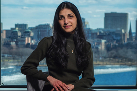 Photo of Ritu Raman seated before a window with Boston’s skyline in the background